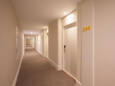 Verlichte hotelgang met lichte muren en kamerdeuren aan de rechterkant.