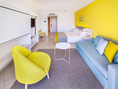 Modern hotelkamer met gele muur, blauwe bank en gele fauteuil.