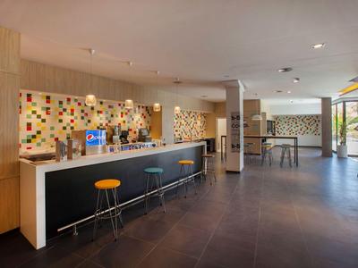 Moderner Hotelbarbereich mit bunten Hockern, langer Theke und großen Fenstern.