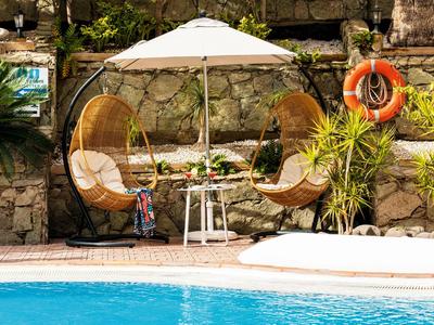 Twee ronde rotan stoelen met kussens onder een witte parasol naast een zwembad.