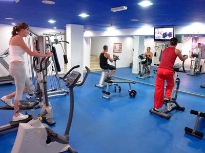 Fitnessruimte met blauwe vloer en meerdere mensen die trainen op apparaten.