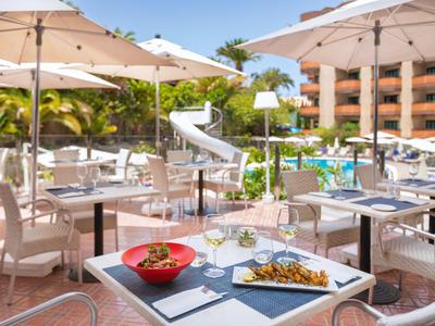 Buitenrestaurant met witte tafels, parasols en uitzicht op zwembad en glijbaan.