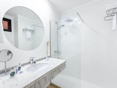 Bright, modern bathroom with round mirror, double sink, and walk-in shower with glass panel.