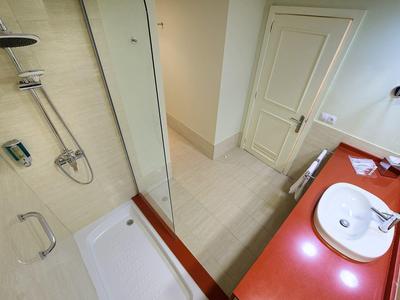 Modern bathroom with a shower, two sinks on a red countertop, and beige tiled floor and walls.