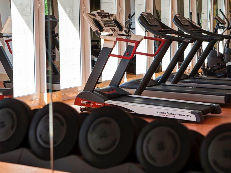 Row of treadmills and dumbbells in a gym with mirrored walls.