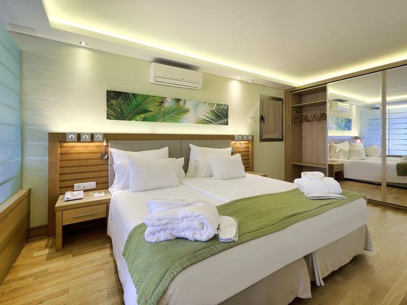 Modern hotel room with two beds, wooden floors, green accents, and large mirror closet.