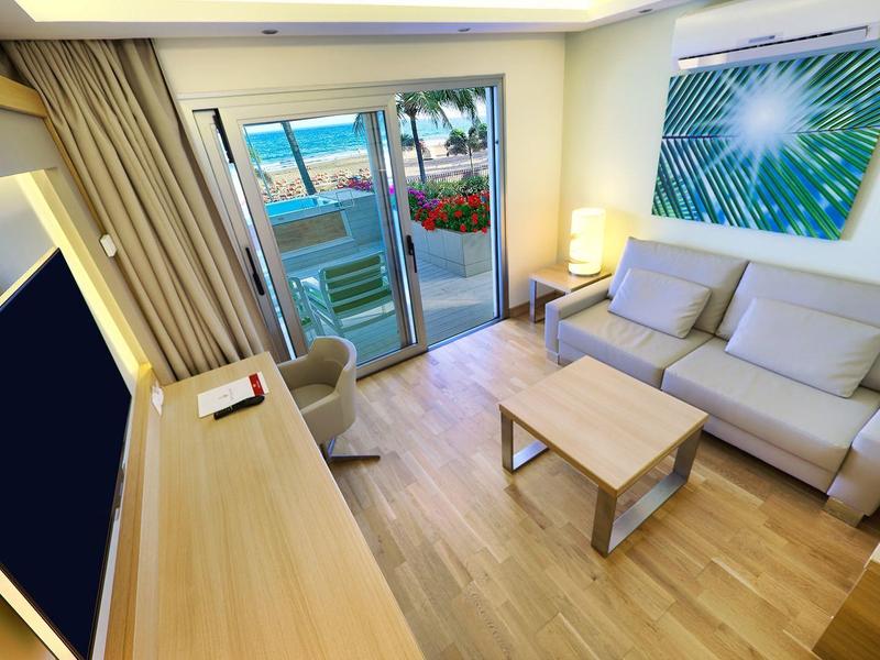 Living room with beige sofa, wooden coffee table, desk, and balcony with ocean view.