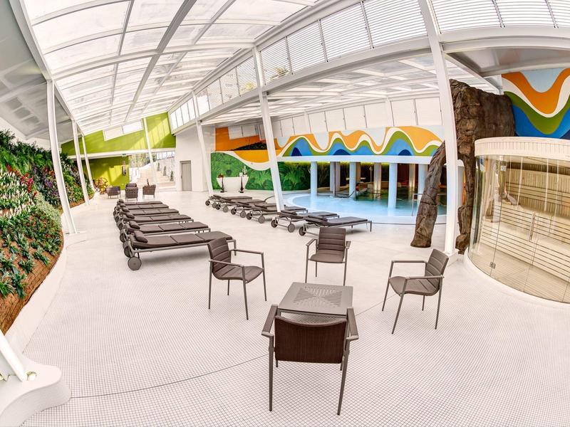 Modern outdoor pool area with lounge chairs, chairs, and colorful wall design.