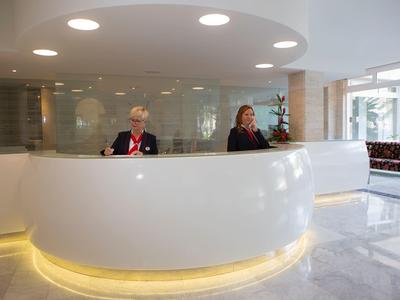 Bright hotel lobby with a round reception desk and two front desk staff.
