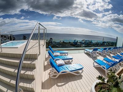 Rooftop terrace with pool, sun loungers, and sea view under cloudy sky.