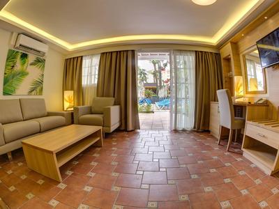 Bright hotel suite with sofa, desk, flat-screen TV, and view of pool area.