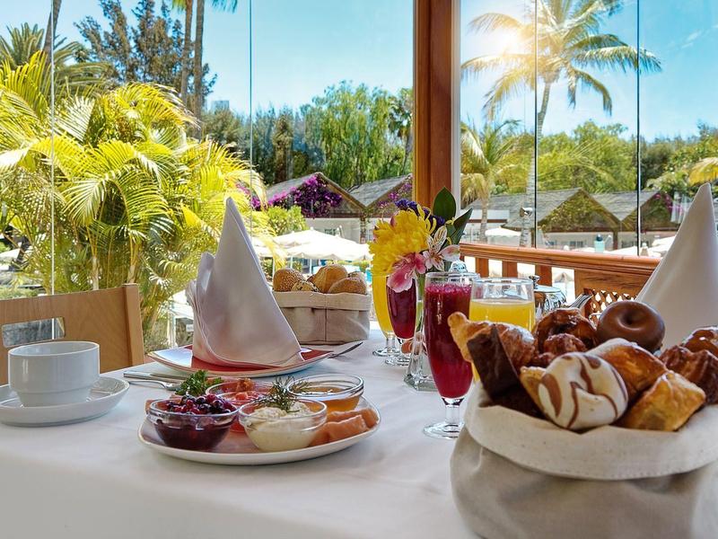 Table set with pastries, macarons, and coffee at an outdoor tropical dining area.