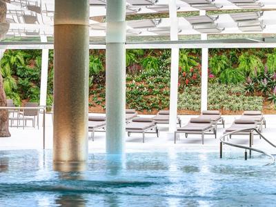 View of a pool with water jets and loungers against a green planted wall in the background.