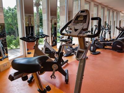 Innenansicht eines Fitnessraums mit mehreren Trainingsrädern vor großen Fenstern und orangem Bodenbelag