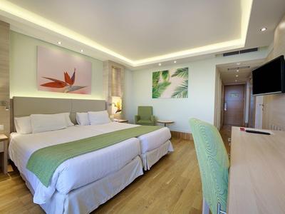 Bright hotel room with twin beds, modern decor, wooden floor, and a large desk with a chair.