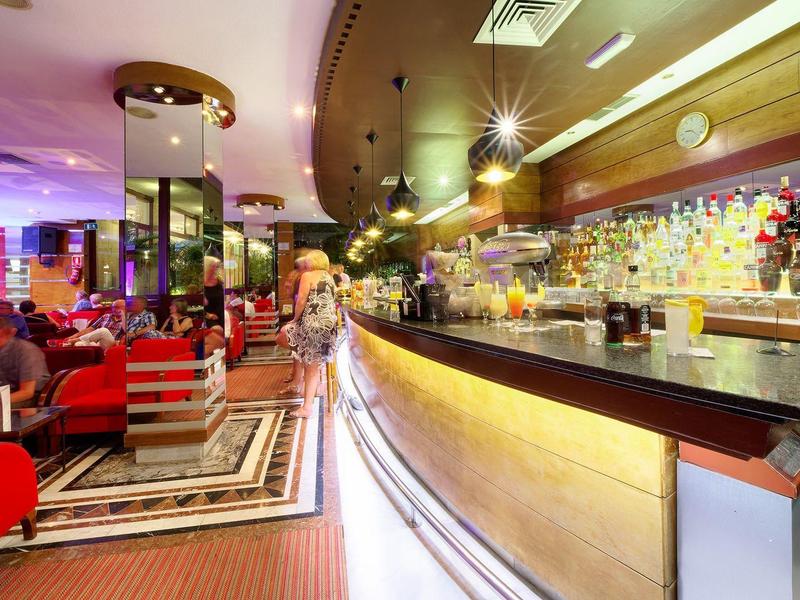 Modern hotel bar with red chairs, well-stocked shelves, and warm lighting ambiance.