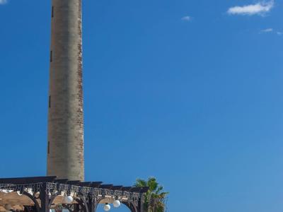 Phare haut sur la côte avec des gens sur une terrasse sous un ciel clair.