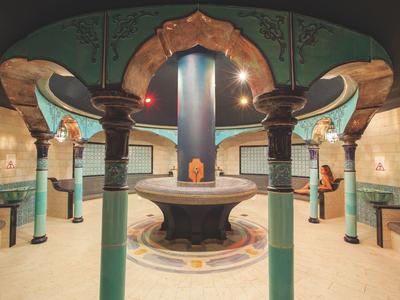 Hammam orné avec colonnes et bassin en pierre central éclairé chaleureusement.