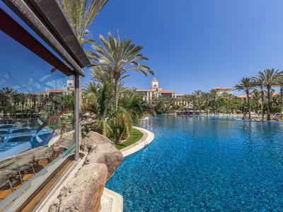 Duży basen na świeżym powietrzu z palmami i budynkami hotelu pod czystym niebem.