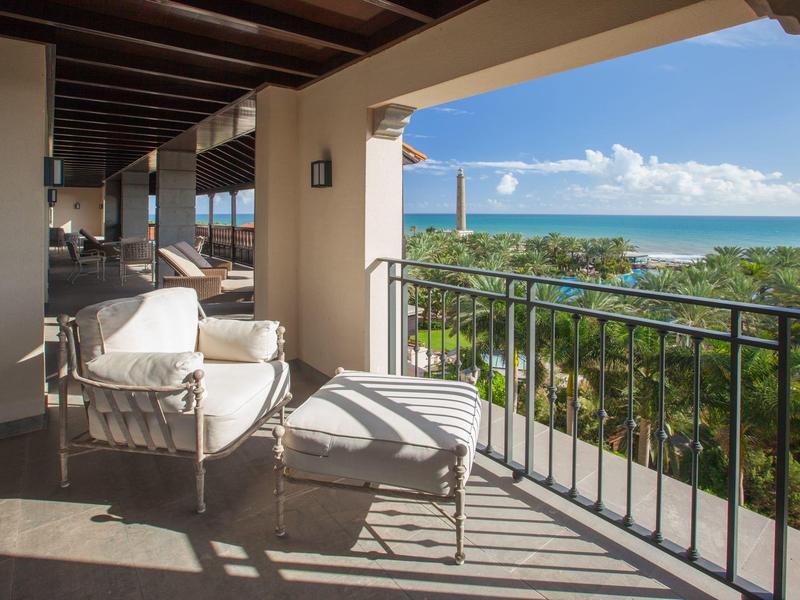 Balcon avec des fauteuils confortables et vue sur la mer sous un ciel bleu.