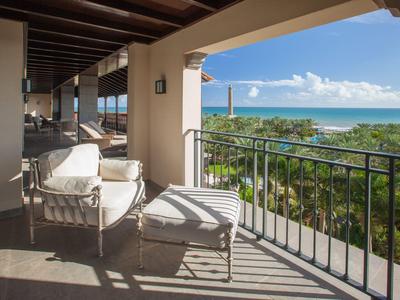 Balcone con poltrona e pouf con vista su palme e mare in una giornata di sole
