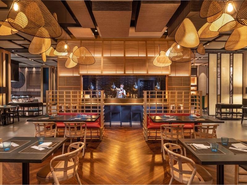 Moderní restaurace s dřevěným stropem a uměleckými lampami v teplém osvětlení.