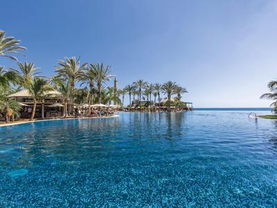 Großer Hotelpool mit Palmen und klarem blauem Himmel am Meer.