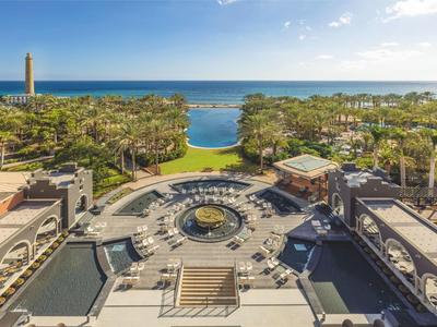 Blick auf ein Resort mit Pool, Garten und Meer im Hintergrund bei klarem Himmel.