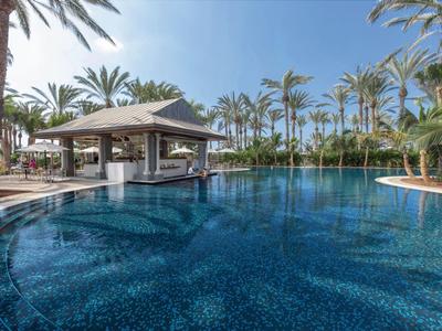 Modern zwembad met swim-up bar en palmbomen onder een heldere blauwe lucht.