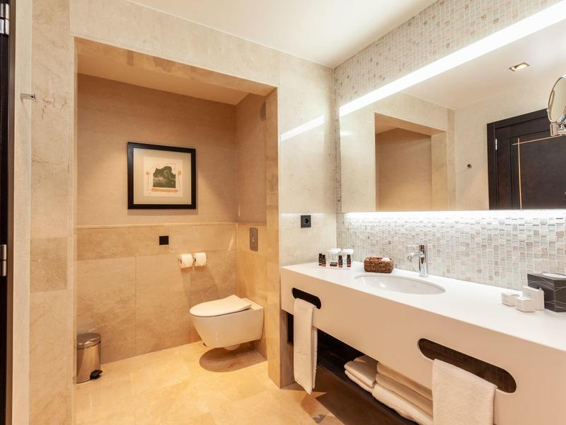 Modern bathroom with large mirror, double sinks, and wall-mounted toilet in warm tones.