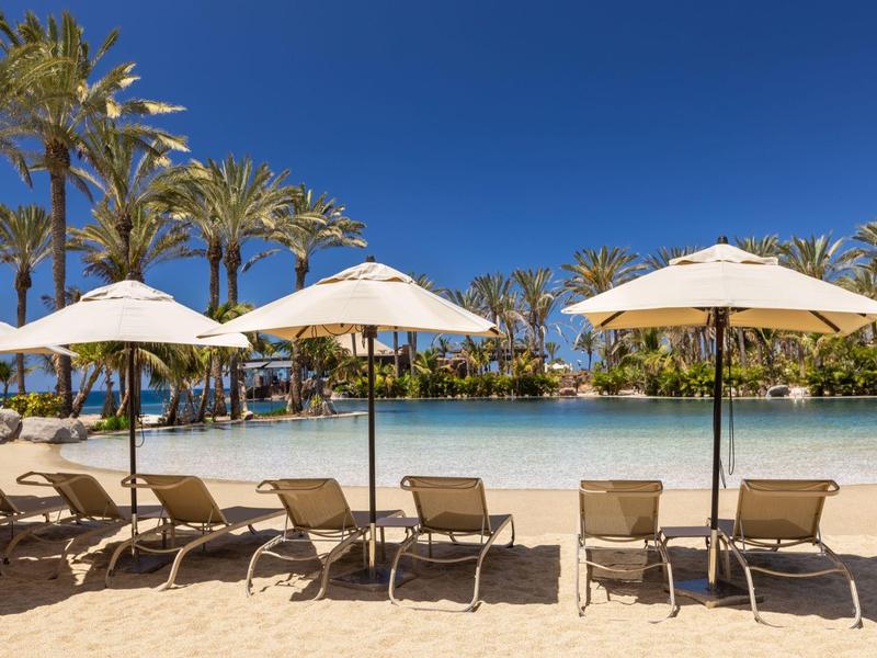 Beachside loungers with umbrellas facing calm blue water under clear sky.