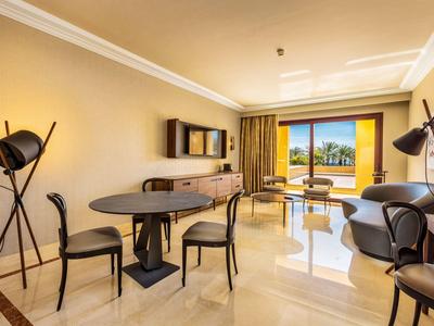 Habitación de hotel luminosa con comedor, asientos y ventana grande con vista.