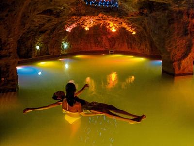 Persona relajándose en una piscina spa iluminada dentro de una cueva de roca natural.