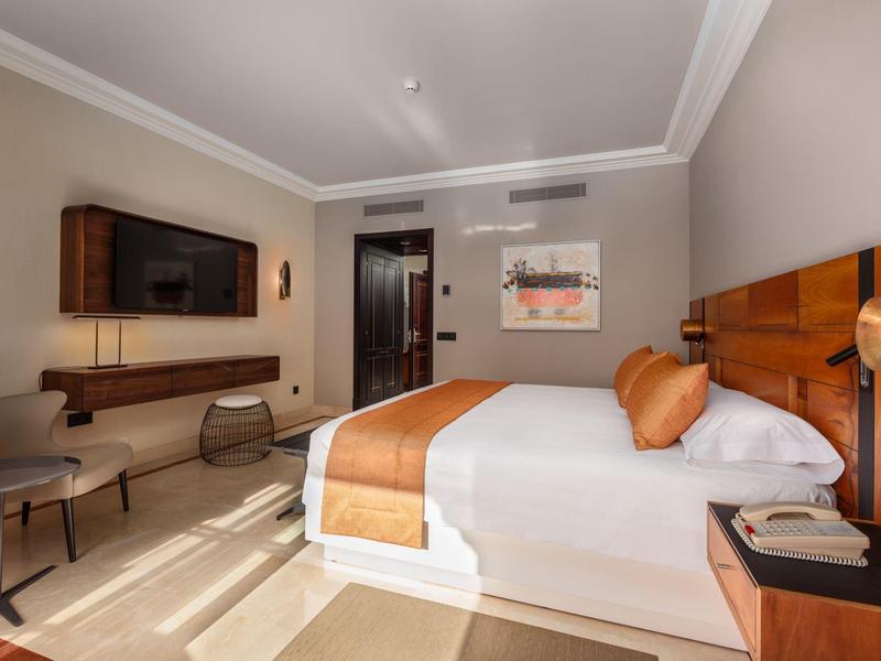 Habitación de hotel luminosa con cama doble, detalles en naranja y decoración moderna.