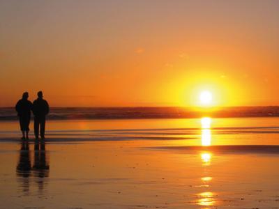 Twee mensen lopen op het strand bij zonsondergang met een oranje lucht.