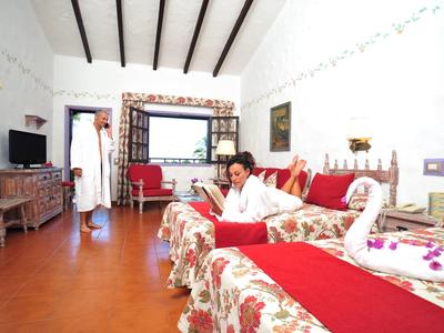 Bright hotel room with two beds, decorated with flowers and towel swan, guest reading.