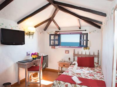 Cozy hotel room with wooden beams, single bed, desk, and sea view through the window.