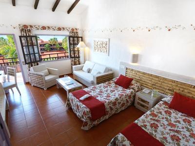 Brightly furnished hotel room with two single beds, sofa, and balcony with a view.