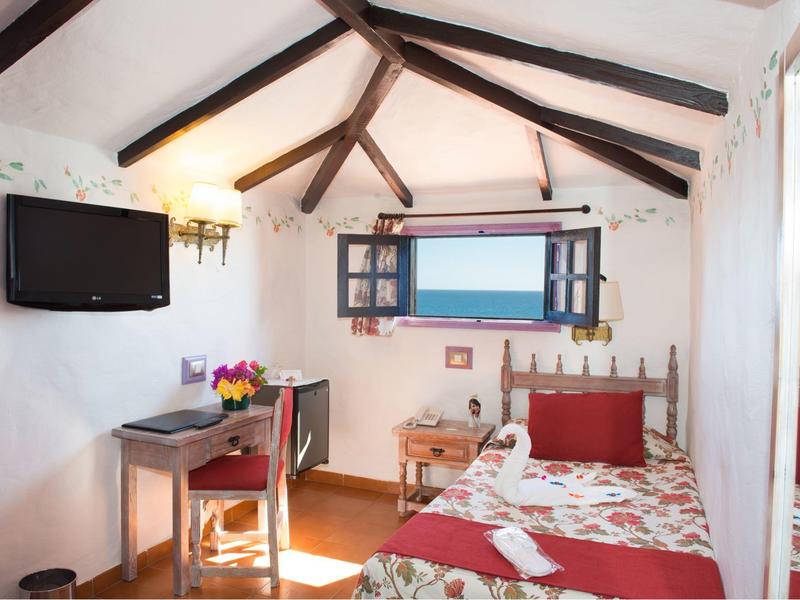 Cozy hotel room with wooden beams, single bed, desk, and sea view through the window.