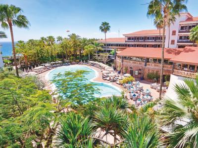 Groot hotel met zwembad, palmbomen en zeezicht op een zonnige dag