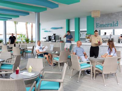 Interno luminoso di un bar d'hotel con ospiti seduti a tavoli e sedie in rattan.