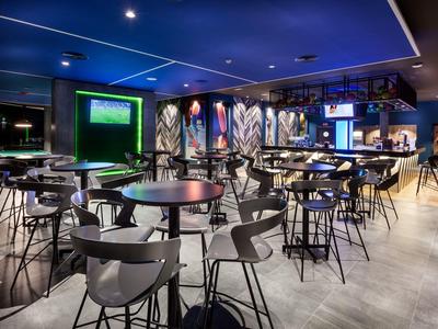 Area bar di un hotel moderno con tavoli alti, sedie e illuminazione di stile.