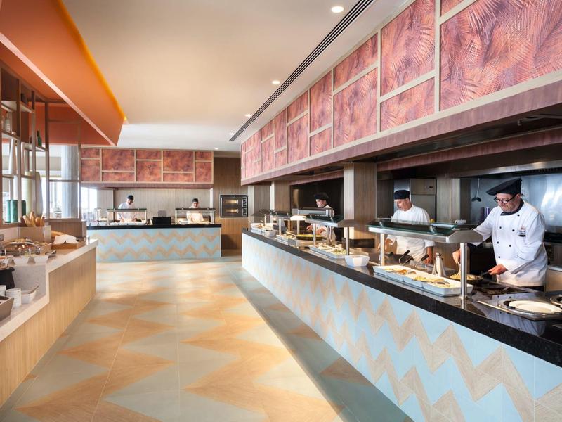 Area buffet moderna in hotel con chef dietro al bancone e interno luminoso.