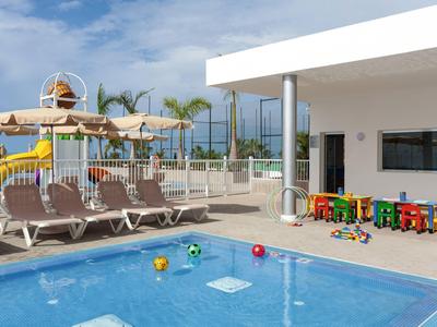 Children's pool with toys next to terrace with loungers and playground at hotel.