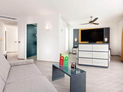 Bright living room with gray sofa, glass table, and large TV on dresser.