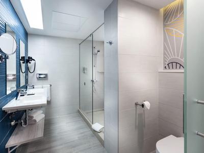 Modern hotel bathroom with glass shower, white sinks, and blue wall tiles.