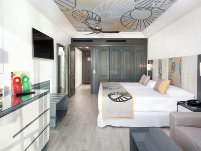 Modern hotel room with double bed, wardrobe, wall art, and light wooden flooring.