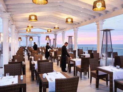 Ristorante elegante con tavoli apparecchiati, sedie in vimini e vista sul tramonto sul mare.
