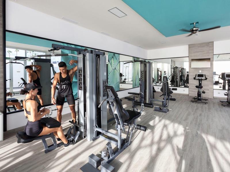 Palestra luminosa con grandi specchi, attrezzi per allenamento e due persone che si allenano.