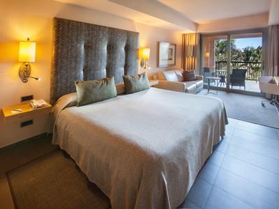 Camera d'albergo luminosa con letto grande, decorazioni eleganti e balcone con vista esterna.